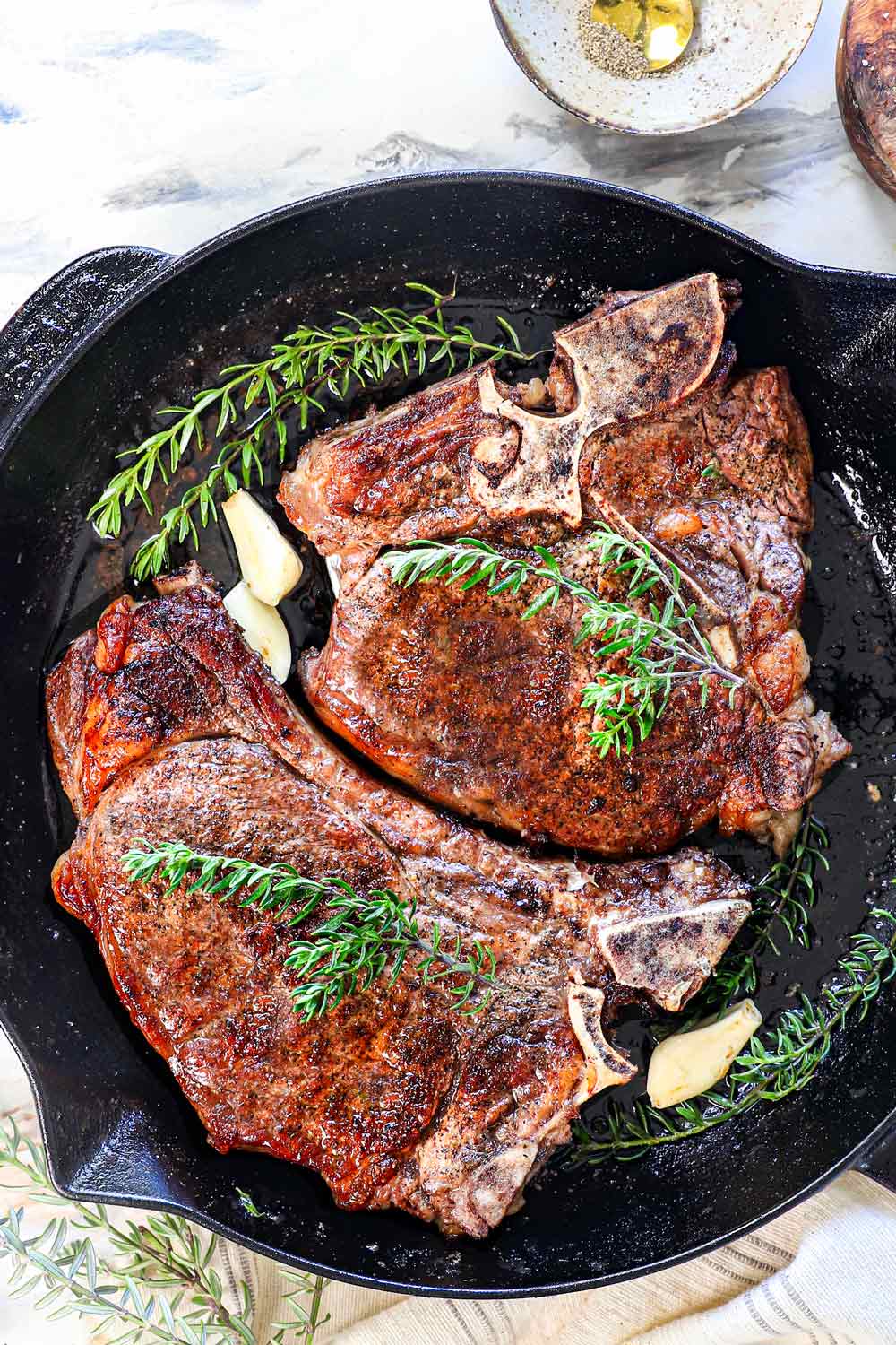 top view of reverse sear steak recipe in a skillet garnished with rosemary