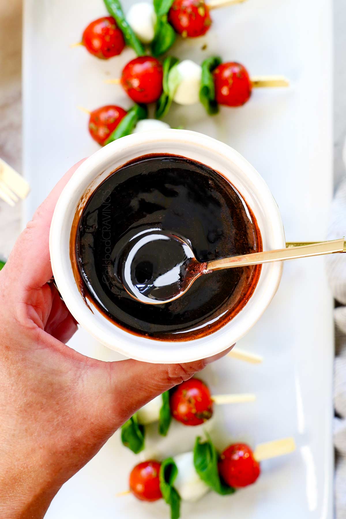 showing how to make caprese skewers by drizzling with balsamic glaze