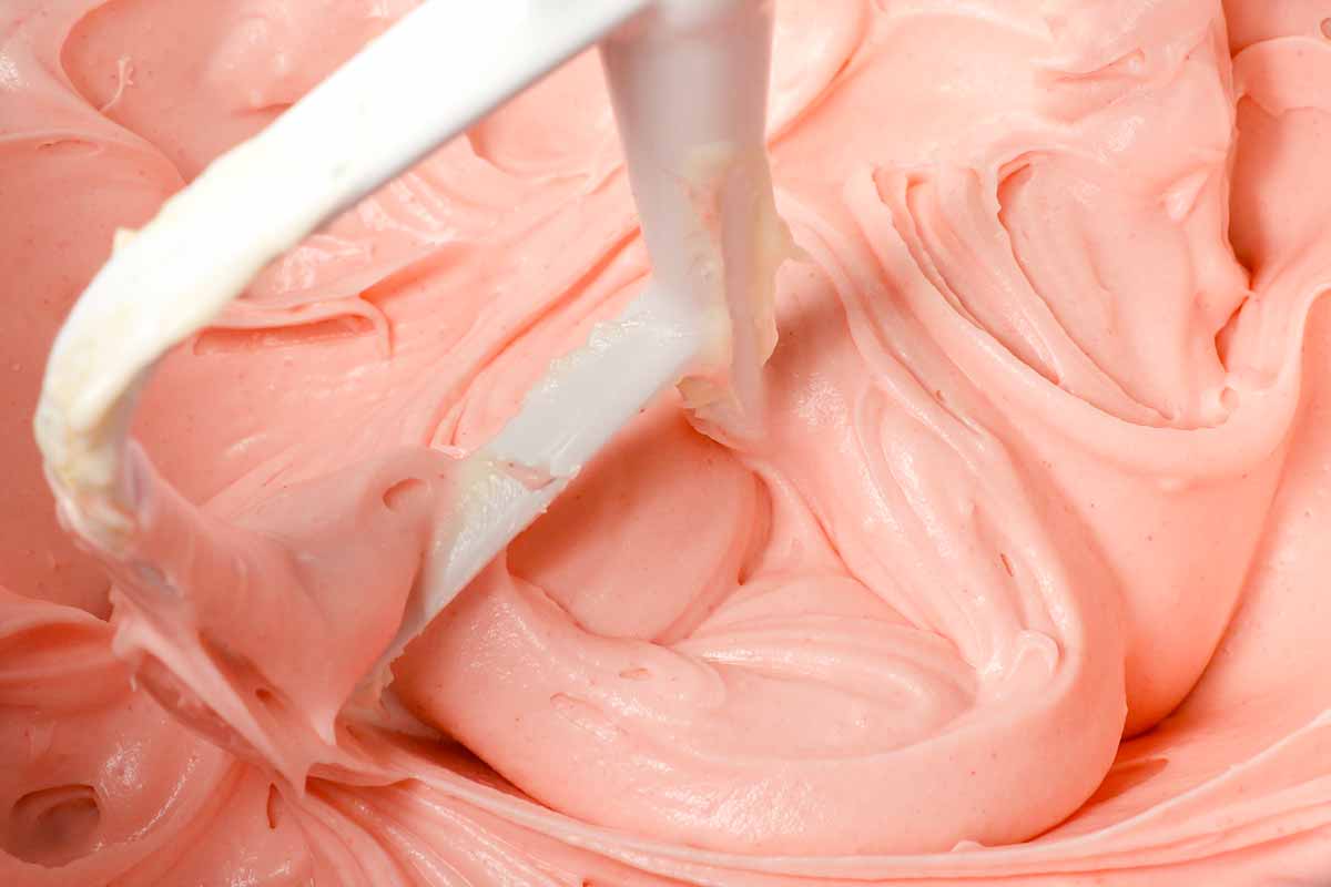 showing how to make strawberry frosting for strawberry cake recipe by beating the cream cheese, butter, powdered sugar, and strawberry gelatin together
