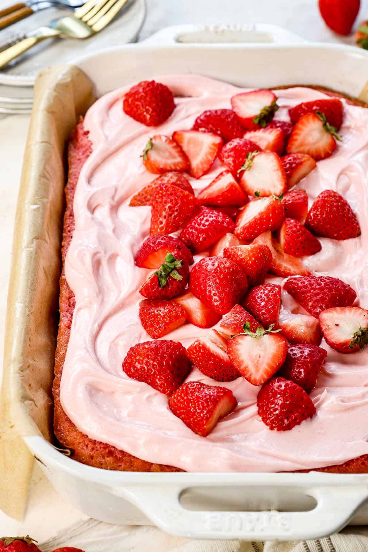 showing how to make strawberry cake recipe by frosting with strawberry cream cheese frosting and topping with fresh strawberries
