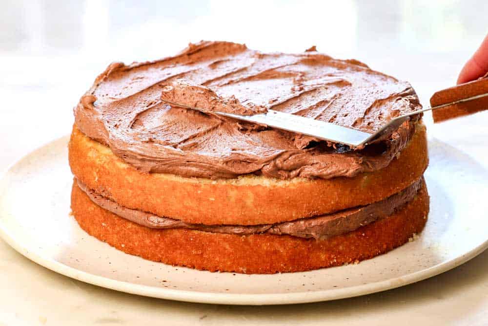 showing how to make yellow cake by frosting the cake with chocolate frosting