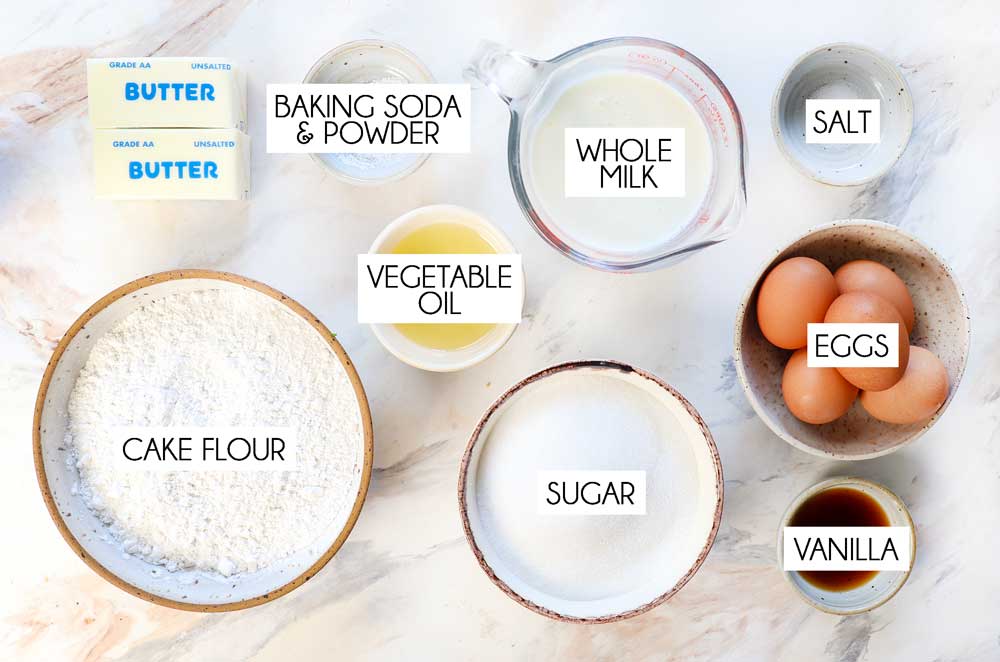 Top view of yellow cake ingredients: cake flour, milk, butter, vegetable oil, baking soda, baking powder, salt, eggs, vanilla