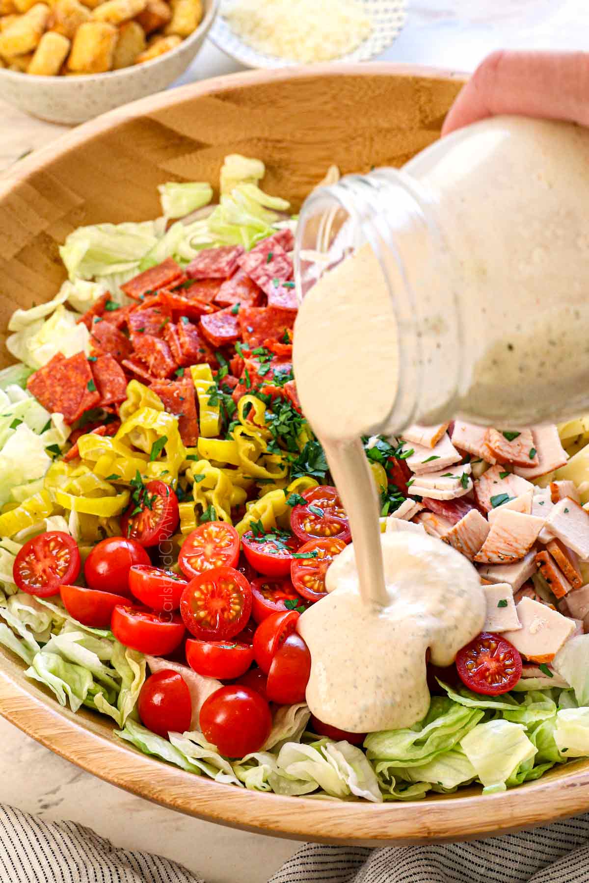showing how to make Grinder salad by pouring the dressing over the salad