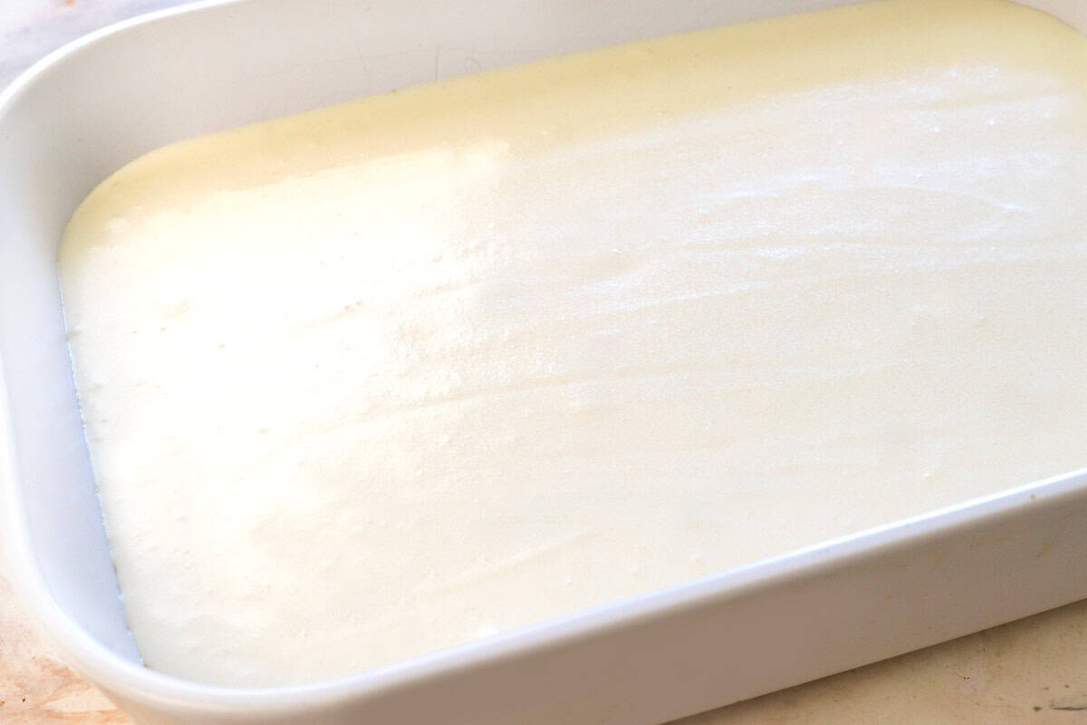 showing how to make strawberry pretzel salad by spreading the cream cheese layer over the pretzel crust