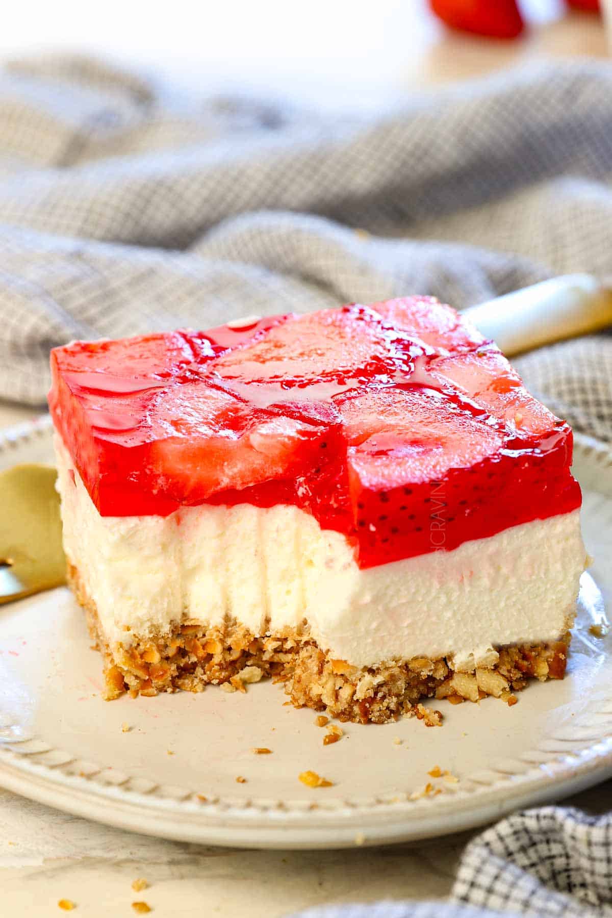 a slice of pretzel and strawberry jello salad on a plate with a bite taken out showing how creamy it is