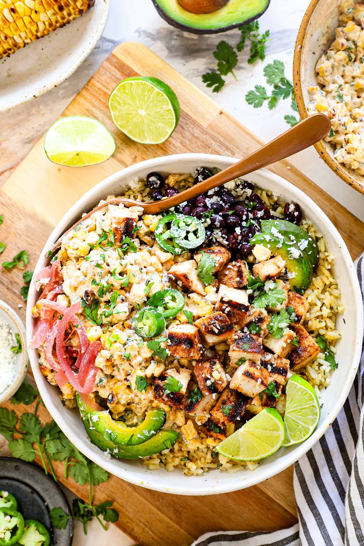 showing how to make street corn chicken rice bowls by adding cilantro lime rice, chicken, Mexican street corn, beans, avocado, lime and jalapeno