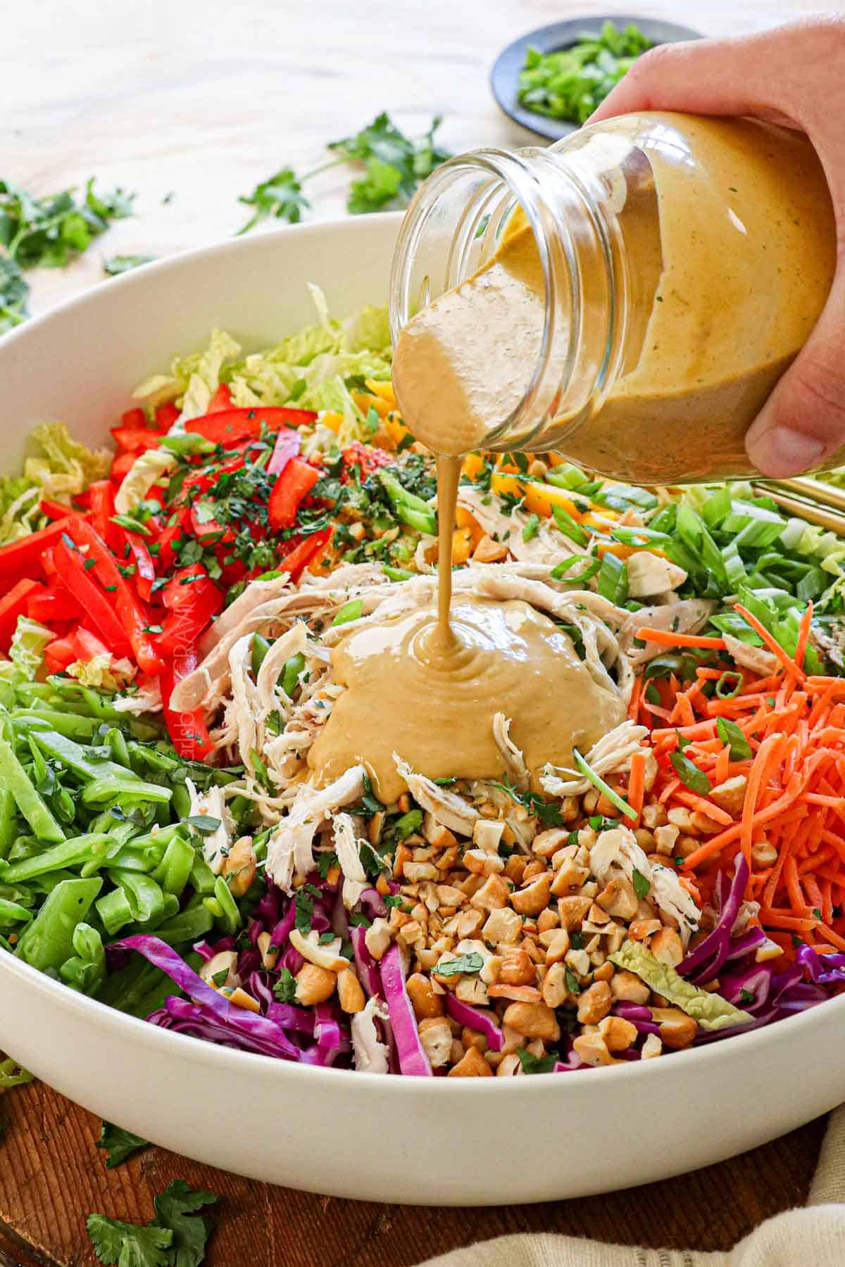 showing how to make Thai Chicken Salad by drizzling with the Thai peanut dressing