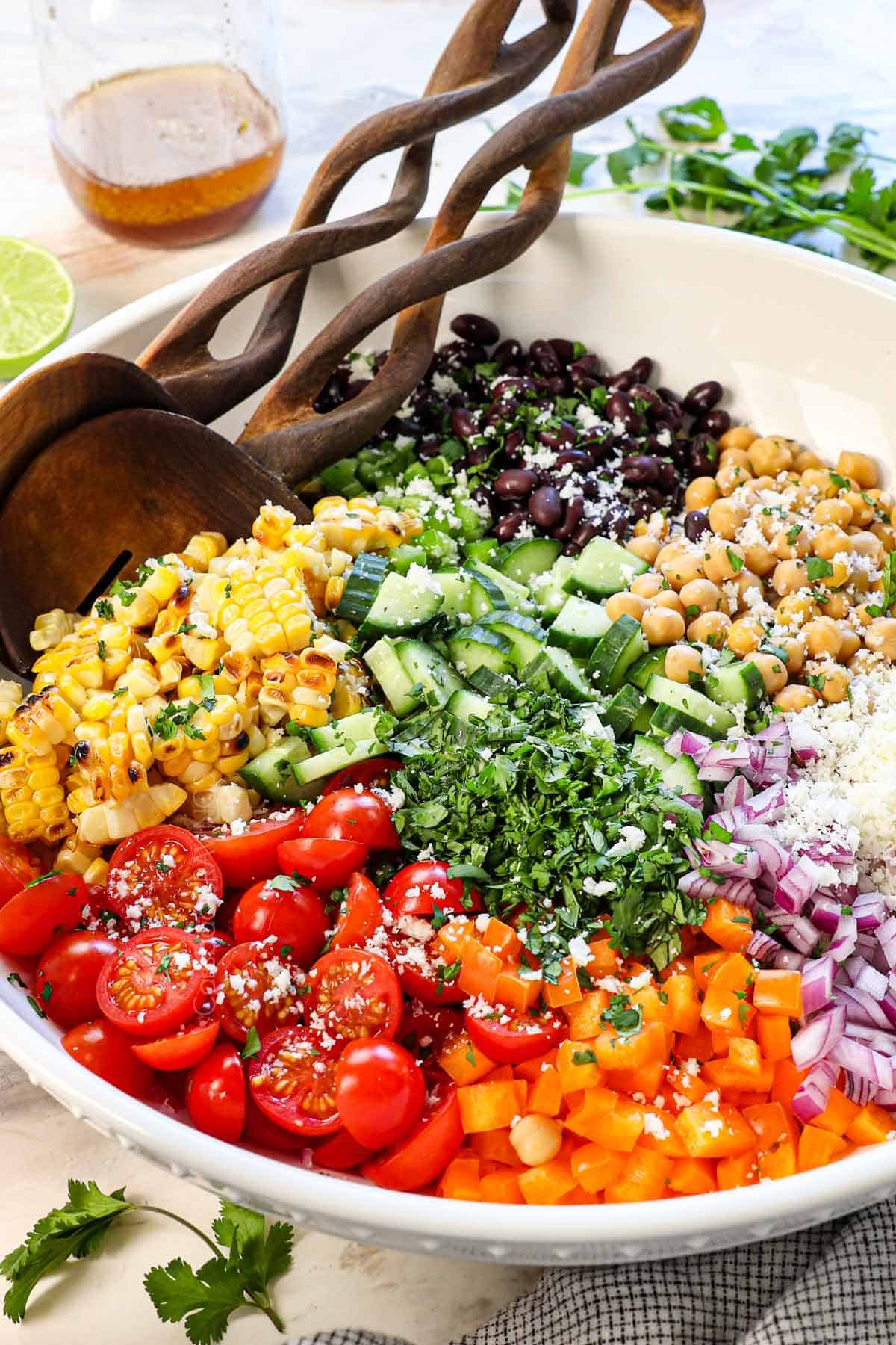 side view of the dense bean salad recipe before it's tossed showing the ingredients of chickpeas, black beans, corn, tomatoes, red onion, bell pepper, cotija and cilantro