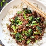 top view of ground beef and broccoli being served over white rice garnished by green onions