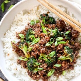 top view of ground beef and broccoli being served over white rice garnished by green onions