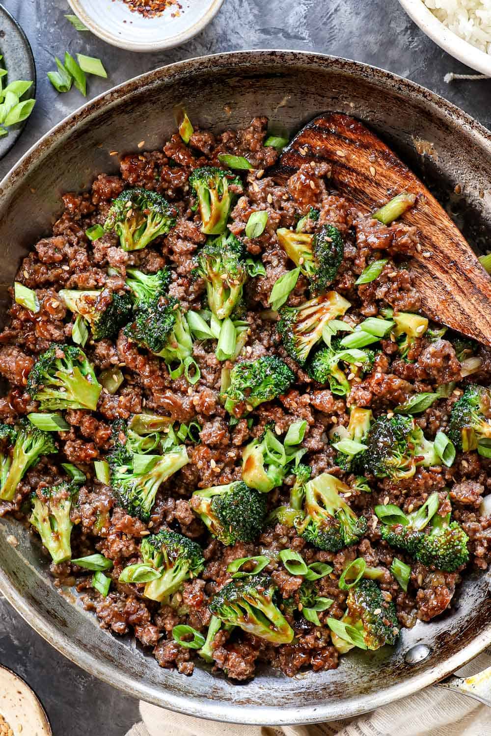 showing how to make ground beef and broccoli by garnishing with green onions and toasted sesame seeds