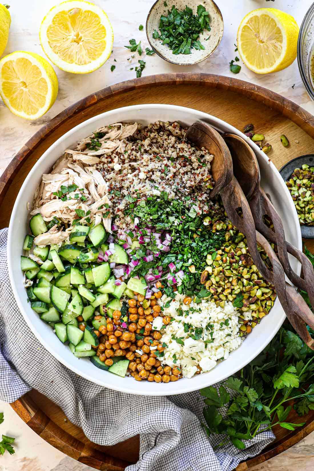showing how to make Jennifer Aniston Salad by adding quinoa, chickpeas, pistachios, feta, red onion, English cucumber, mint, parsley to a large bowl