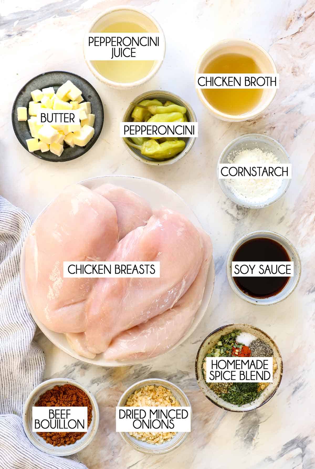 top view of Mississippi chicken ingredients: chicken breasts, butter, pepperoncini, pepperoncini juice, soy sauce, beef bouillon, chicken broth, cornstarch, dried herbs and spices