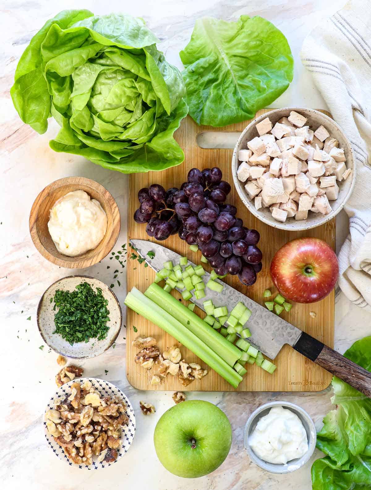 top view of waldorf salad ingredients: chicken, grapes, celery, apples, walnuts, mayonnaise, yogurt, parsley, dill, sugar, red wine vinegar