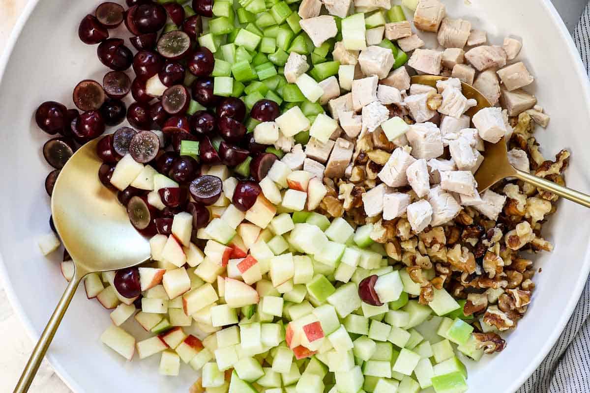 showing how to make waldorf salad by adding the grapes, celery, chicken, apples, and walnuts to a bowl