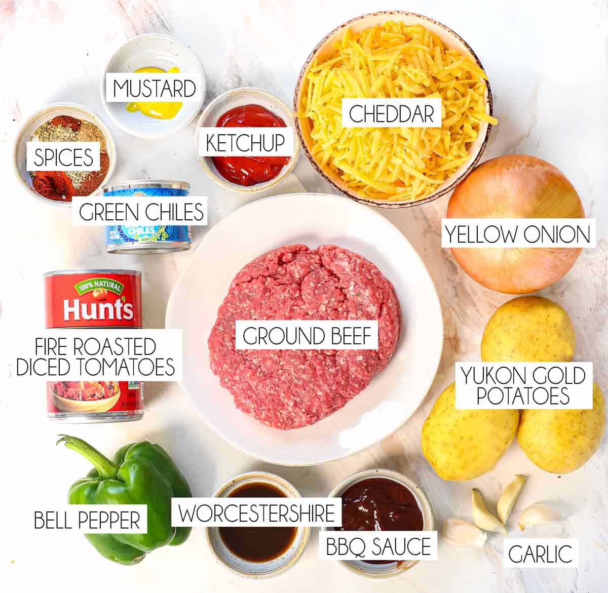 top view of ground beef and potatoes ingredients: ground beef, yukon gold potatoes, onion, cheddar, diced tomatoes, green bell peppers, barbecue sauce, ketchup, mustard, spices