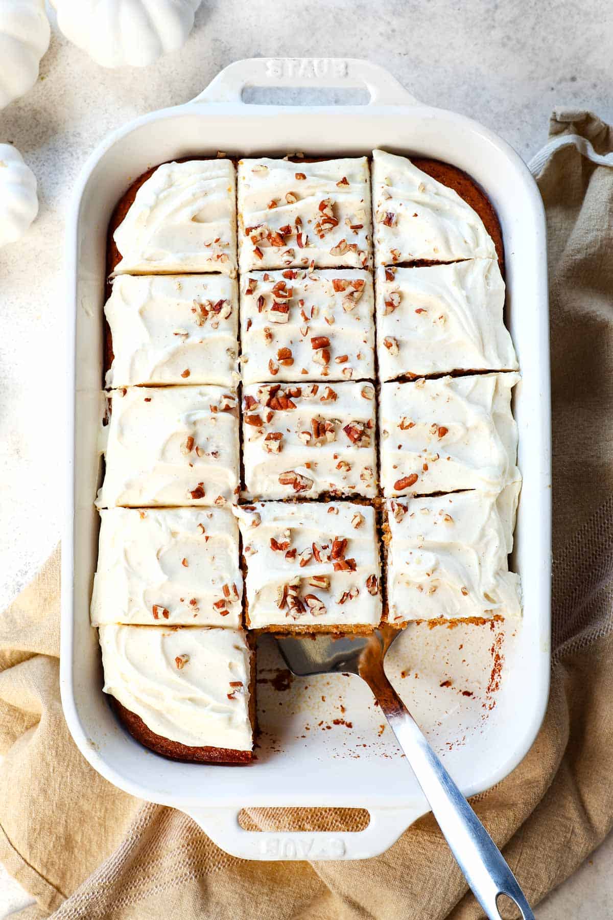 showing how to make pumpkin cake by frosting with cream cheese frosting and garnishing with pecans