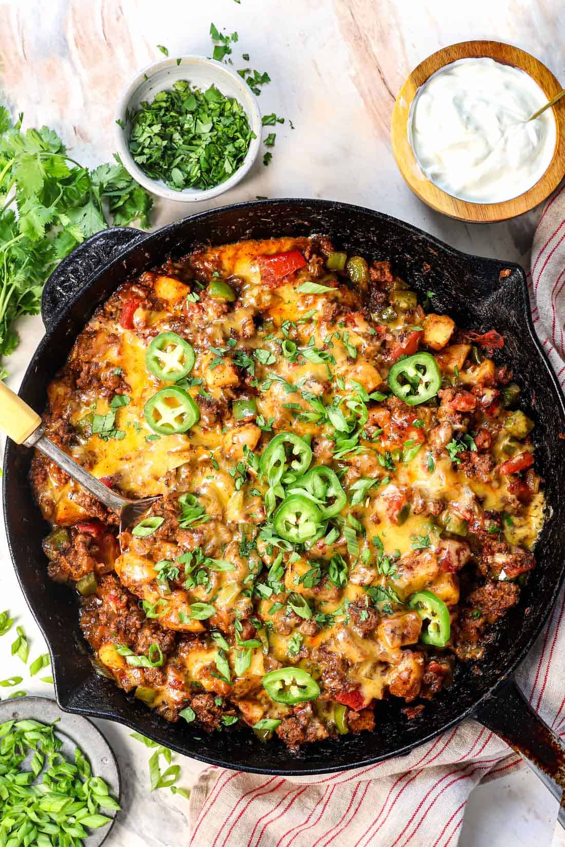 showing how to make ground beef and potatoes by garnishing with jalapeños, green onions, and cilantro