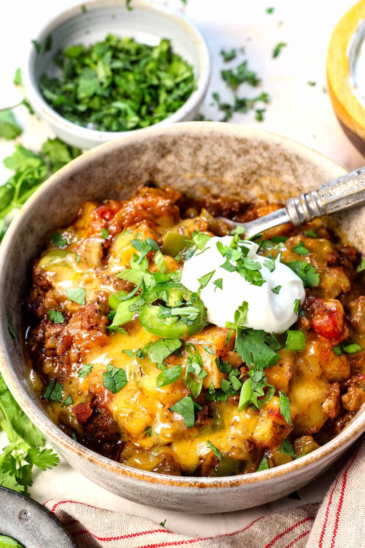 ground beef and potato recipe being served in a bowl garnished by green onions with a dollop of sour cream
