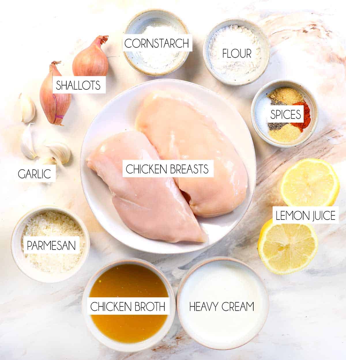 top view of lemon chicken ingredients: chicken breasts, fresh lemon juice, chicken broth, heavy cream, flour, cornstarch, shallots, garlic, spices
