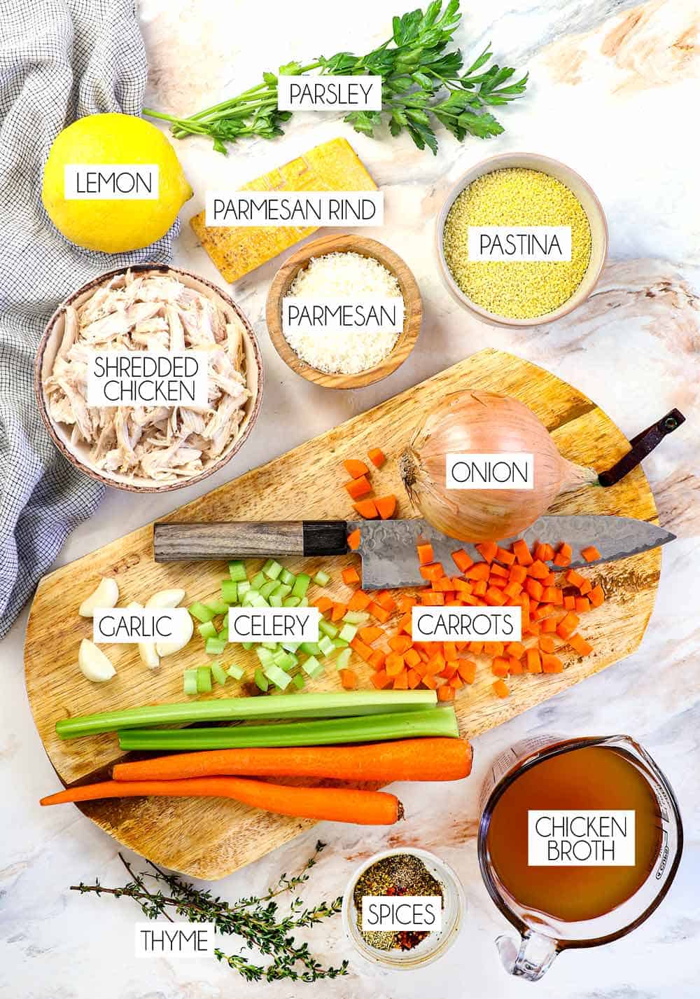 top view of penicillin soup (pastina soup) ingredients: carrots, celery, onions, garlic, chicken broth, pastina pasta, Parmesan rind, shredded Parmesan, shredded chicken, lemon